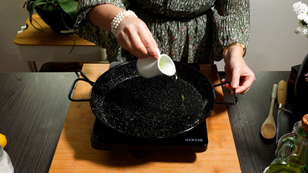 Numa paelheira (paellera - recipiente próprio para confecionar paella), colocar um fio de óleo, os dentes de alho picados.